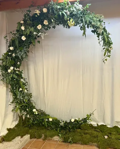 Arche de mariage circulaire couverte de feuillage dense et de fleurs blanches, posée sur un tapis de mousse