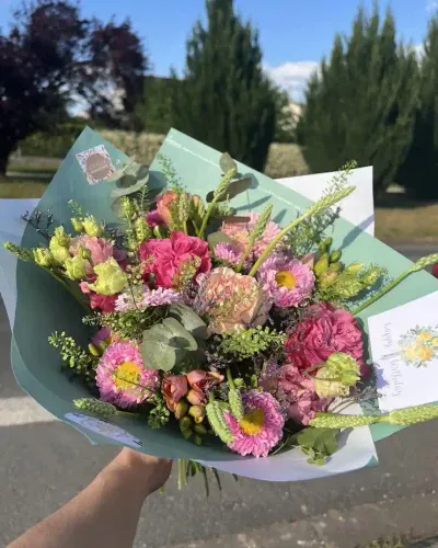 Bouquet de roses roses, asters, lisianthus et œillets pêche avec des graminées, dans un papier vert d'eau
