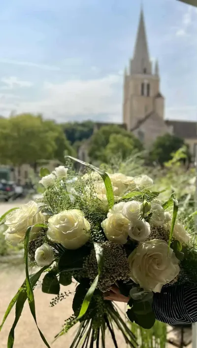 Bouquet de roses blanches et de feuillages légers tenu à la main, le clocher de Saint-Benoît en arrière-plan