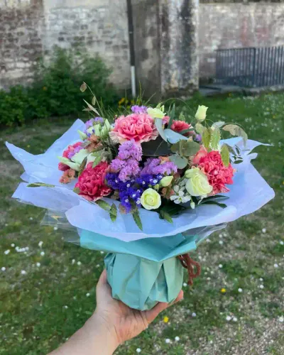 Bouquet bulle d'œillets roses, statice violet, roses blanches et eucalyptus, emballé de vert d'eau, tenu à la main