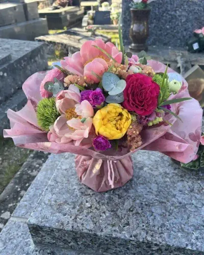 Bouquet bulle de pivoines corail, rose rouge, rose jaune et œillets, déposé sur une tombe en granit