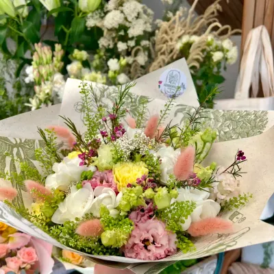 Bouquet de freesias blancs, lisianthus roses, œillet jaune et queues de lièvre roses dans un papier kraft