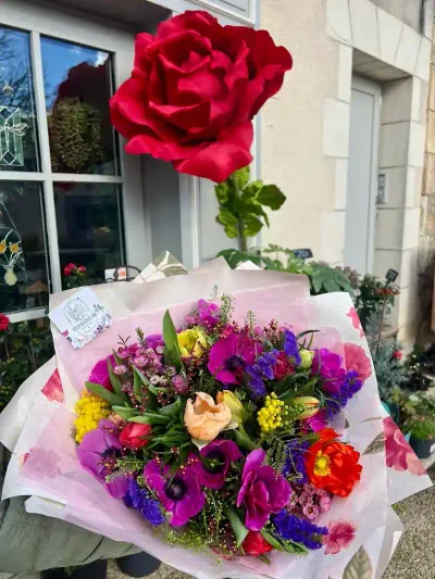 Bouquet d'anémones violettes, renoncules, mimosa et roses devant la vitrine Herborium, sous une rose géante rouge
