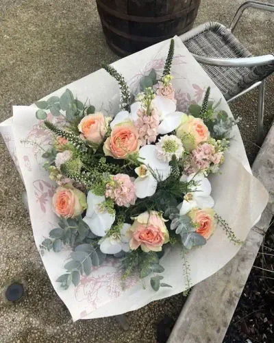 Bouquet de roses pêche, orchidées blanches, giroflées roses, véroniques et eucalyptus dans un papier imprimé