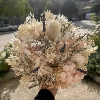 Bouquet de fleurs séchées aux tons beige et rose poudré, avec pampa, lavande et chardons blanchis, tenu à la main
