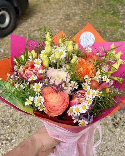 Bouquet de renoncules saumon, tulipes, camomille et lisianthus verts dans un papier rose et orange vif