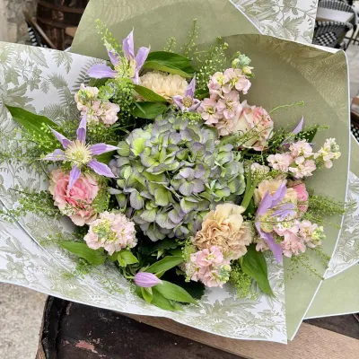 Bouquet pastel d'hortensia vert et mauve, giroflées roses, œillets et clématites mauves dans un papier imprimé