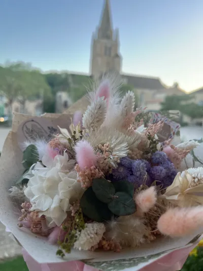 Bouquet de fleurs séchées pastel : hortensia blanc, queues de lièvre roses, fleurs violettes et eucalyptus, devant l'église