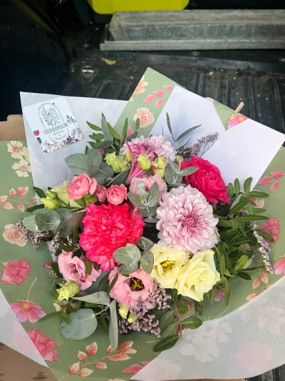 Bouquet rond de dahlias roses, roses jaunes, œillets fuchsia et lisianthus, emballé dans un papier fleuri