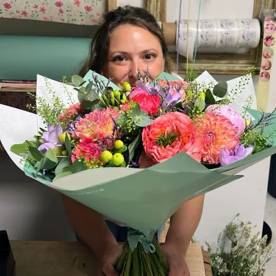 Bouquet généreux de dahlias corail, roses rouges et feuillages, tenu par Léa dans l'atelier Herborium