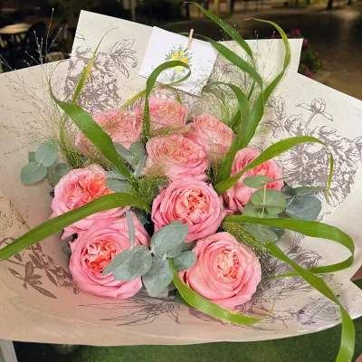 Bouquet de roses de jardin roses, eucalyptus et longues herbes, emballé dans un papier imprimé de fleurs