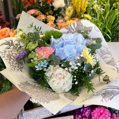 Bouquet d'hortensia bleu, roses blanches, œillets roses et petites fleurs bleues, devant l'étal de la boutique
