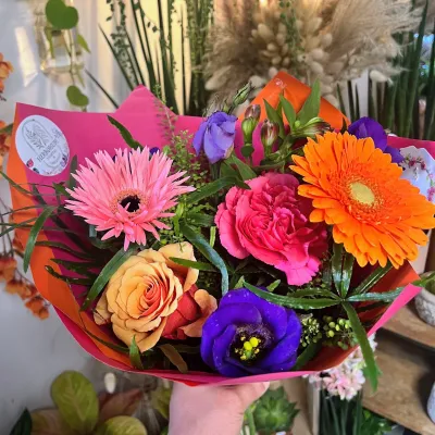 Bouquet vif de gerberas orange et roses, roses fuchsia et lisianthus violets, dans un papier rose fuchsia