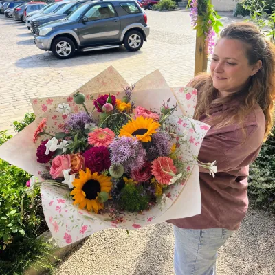 Bouquet champêtre de tournesols, alliums, dahlias et roses, tenu par Léa devant la boutique Herborium