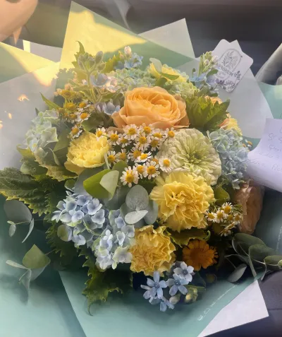 Bouquet pastel d'hortensia bleu, œillets jaunes, rose pêche et matricaire, dans un papier vert d'eau