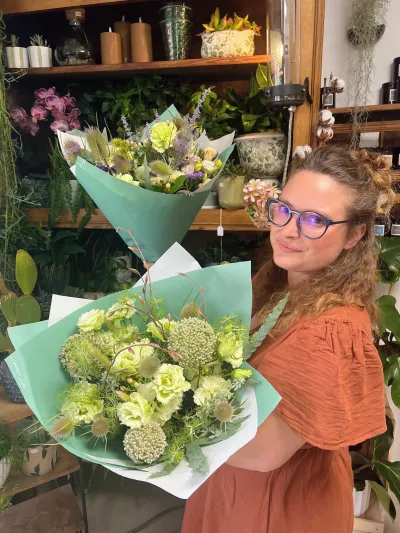 Bouquets blanc et vert aux fleurs rondes et vertes, tenus par Léa parmi les plantes de la boutique Herborium