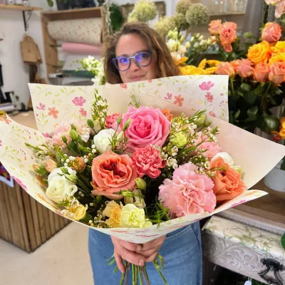 Grand bouquet de roses pêche et roses, œillets roses et fleurs blanches, tenu par Léa dans la boutique Herborium