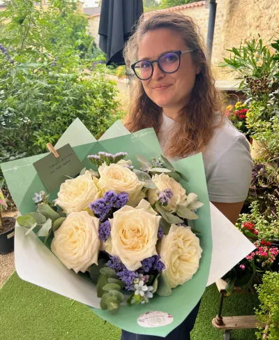 Bouquet de roses blanches et statice violet dans un papier vert d'eau, tenu par Léa dans un jardin