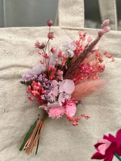 Petit bouquet de fleurs séchées roses et de pampas accroché à un tote bag en toile, avec un ruban d'Octobre rose