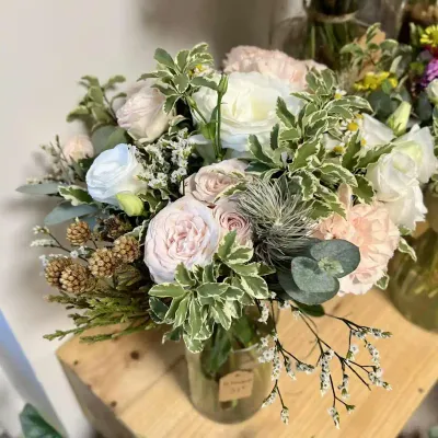 Bouquet en vase de roses blanches et poudrées, feuillage panaché, eucalyptus et tillandsia, sur une étagère en bois
