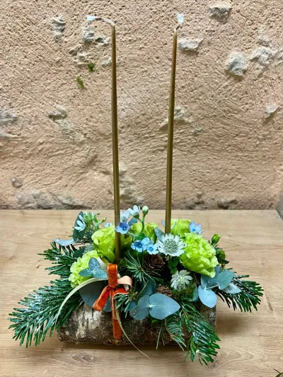 Centre de table de Noël sur rondin de bouleau : sapin, eucalyptus, œillets verts et deux grandes bougies dorées