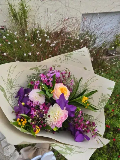 Bouquet de dahlias blancs, orchidées vanda violettes, roses pêche et wax flower, posé sur un massif de fleurs