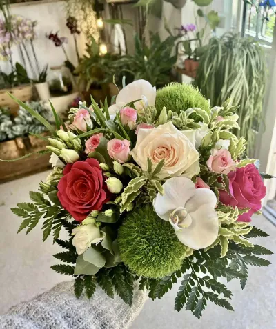 Composition de roses rouge, fuchsia et pêche avec une orchidée blanche et des œillets boules verts, en boutique