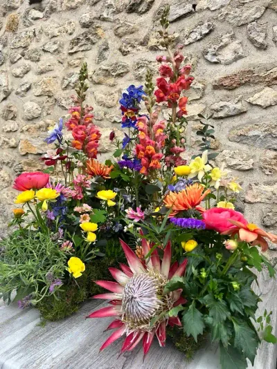 Composition jardin de protea, mufliers, delphiniums, renoncules et boutons d'or contre un mur de pierre