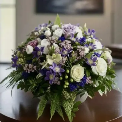 Coussin de deuil rond de roses blanches et mauves, clématites violettes, statice, millepertuis vert et fougères