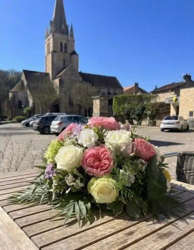 Coussin de deuil rond de roses blanches et roses, lisianthus et feuillage, posé sur une table en bois en extérieur