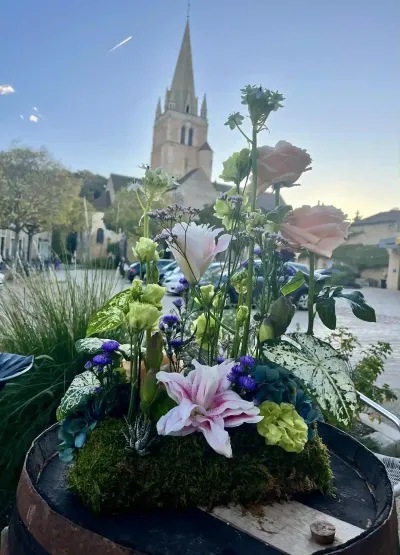Composition sur mousse de lys roses, roses pêche et caladiums, posée sur un tonneau devant l'église de Saint-Benoît