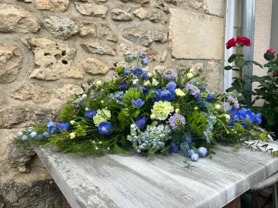 Dessus de cercueil champêtre bleu et vert : delphiniums, scabieuses, hortensia bleu pâle et œillets verts, sur une table