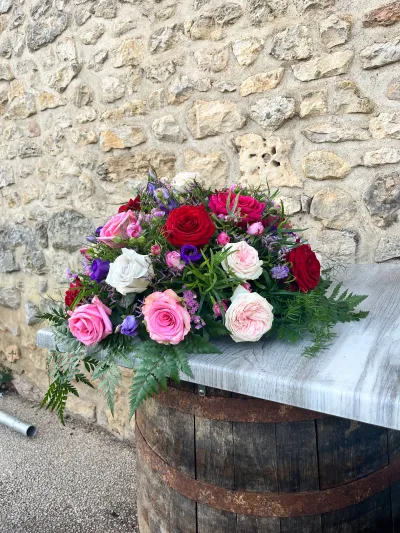 Coussin de deuil de roses rouges, roses et blanches, lisianthus violets et fougère, sur un tonneau devant un mur de pierre