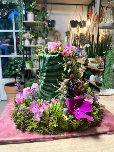 Chapeau haut-de-forme fleuri pour un deuil : feuille verte enroulée, roses, orchidée vanda mauve, mousse, chez Herborium