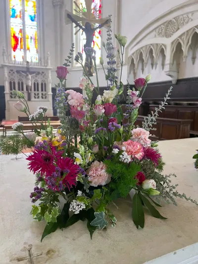 Devant de cercueil coloré de gerberas fuchsia, œillets pêche et mufliers, posé dans une église aux vitraux