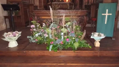Devant de cercueil champêtre, long et bas, au pied de l'autel d'un temple, entre deux bouquets blancs et roses