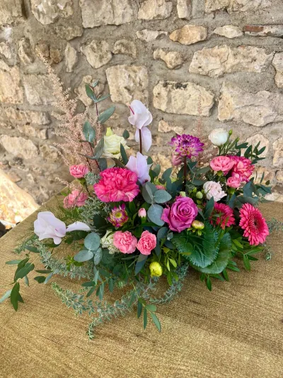 Composition de deuil sur mesure de cyclamens, œillets roses, gerberas fuchsia, rose mauve et dahlia, sur une table en bois