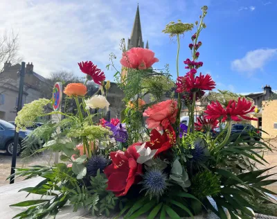 Devant de cercueil coloré de roses rouges, gerberas et chardons bleus, devant l'église de Saint-Benoît