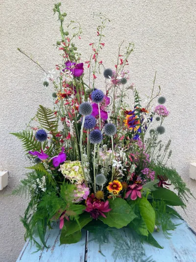Composition de deuil champêtre et haute : chardons bleus, fougères, fleurs des champs roses et orange
