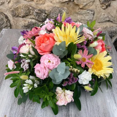 Coussin de deuil rond aux gerberas jaunes, roses corail et roses, lisianthus et eucalyptus, devant la pierre