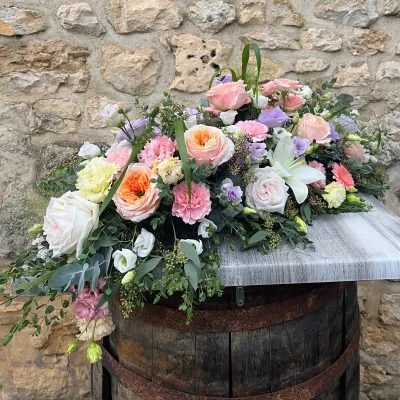 Dessus de cercueil pastel de roses pêche et roses, lys blanc et lisianthus mauves, posé sur un tonneau