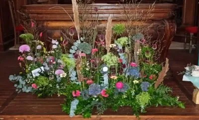 Devant de cercueil champêtre de fleurs des champs, graminées et eucalyptus, au pied de l'autel d'une église