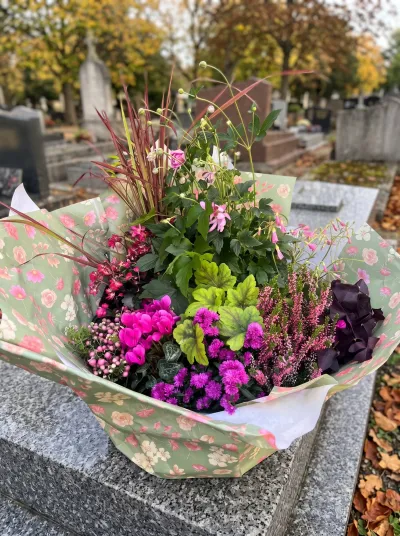 Coupe de plantes de deuil emballée, bruyère, cyclamens et feuillages pourpres, posée sur une tombe en granit en automne