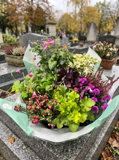 Coupe de plantes d'automne emballée, heuchère vert tendre, oxalis pourpre et bruyère, posée sur une tombe en granit