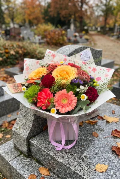Bouquet de deuil coloré à poser, gerbera saumon, roses orange et œillets rouges, debout sur une tombe en granit