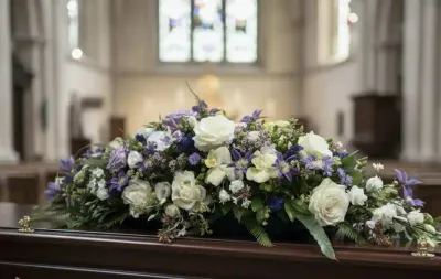 Dessus de cercueil de roses blanches, lisianthus et fleurs mauves et bleues, posé sur un cercueil en bois sombre