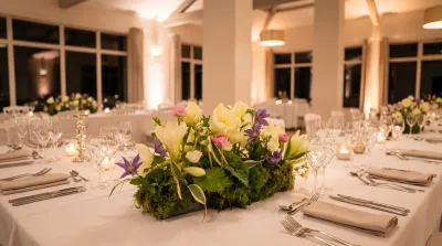 Mise en situation d'une composition de Léa : lys crème, clématites et mousse au centre d'une table de dîner dressée