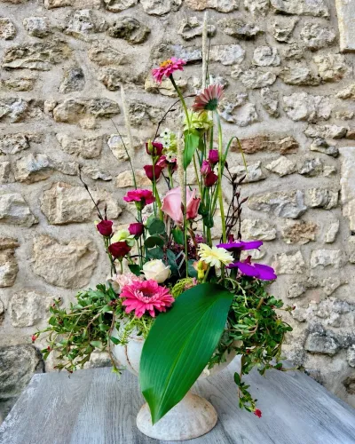 Composition florale dans une vasque blanche : gerberas fuchsia, œillets, orchidées violettes et grande feuille