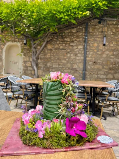 Centre de table végétal : cylindre de feuilles, orchidées fuchsia, roses roses et mousse, sur une terrasse