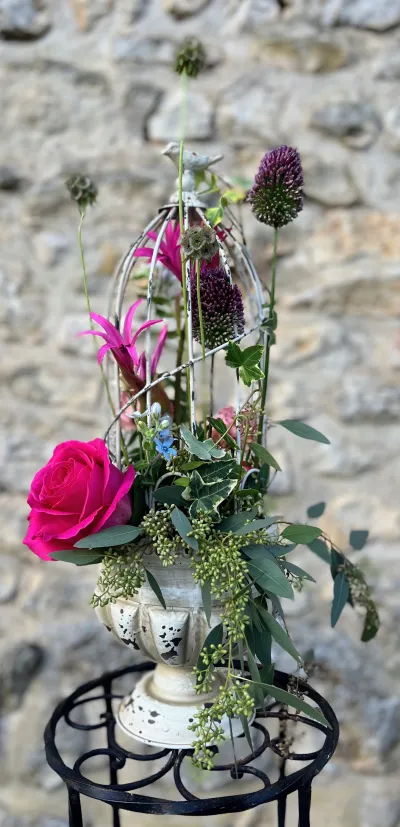 Composition dans une vasque à cage sur un pied en fer forgé : rose fuchsia, alliums et feuillage léger